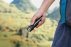 Olightの黒いOclip Proハンディライトを片手で持ち、豊かな自然の山々を背景に登山やアウトドア、ハイキングで携帯する使用シーン