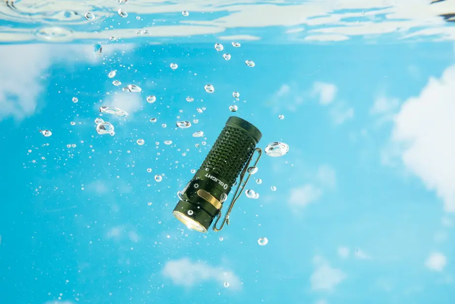 水中の緑のOlight防水懐中電灯、泡立つ水と青空の反射