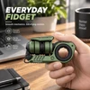 GoBiggeRのグリーン色のメタル製フィジェットトイを手に持つ様子。デスクの上のノートやPC、観葉植物を背景に、スムーズな回転やストレス解消機能を説明する英語テキストが添えられたおしゃれな商品紹介画像。
