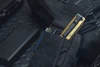 Olight ArkProのビンテージゴールド懐中電灯。黒いポーチにクリップで収納された状態。アウトドアやEDC向けのポータブルライト。