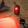 図面の上で赤色光を照射するOlightの黒い小型LEDクリップライトOclip Pro。夜間の読書や精密作業、暗所での手元を照らす作業灯として最適です。