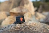 岩の上に設置された黒いOlight Osight SEタクティカルドットサイト、RMRからRMScへのアダプターを装着した斜めからの外観、アウトドアや狩猟、射撃トレーニングに最適な高耐久の光学照準器