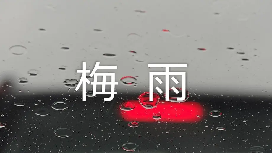 「梅雨」の文字、車の窓に付いた雨粒、ぼやけた赤いテールランプ。
