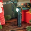 黒い懐中電灯が木製のテーブルに置かれ、クリスマスプレゼントと針葉樹の枝が飾られている。