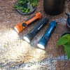 Olightのオレンジ、ブラック、ブルーのSeeker 4 Pro懐中電灯は、キャンプやアウトドアで強力な光を放ちます。