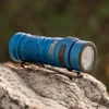 青いBaton 3懐中電灯、岩の上にクリップで固定され、屋外背景に植物模様が見える。
