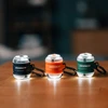 GOBERの黒、オレンジ、緑のキャンプ用ランタン、木製テーブル上で光る3つ