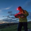 ヘッドランプをつけたハイカーが夜明けの丘で地図を読んでいる