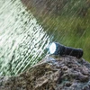 雨が降る中で岩の上に置かれた光る防水懐中電灯