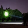 夜に懐中電灯で木を照らす男性、暗闇の中、明るい光が広がる