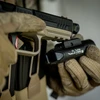 Olight PL Turbo Valkyrieウェポンライト。タクティカルグローブを装着した手が、ライフルに取り付けられたPL Turbo Valkyrieの側面から、その堅牢なデザインと安全性を捉えています。銃器用ライトとしての用途に適しています。